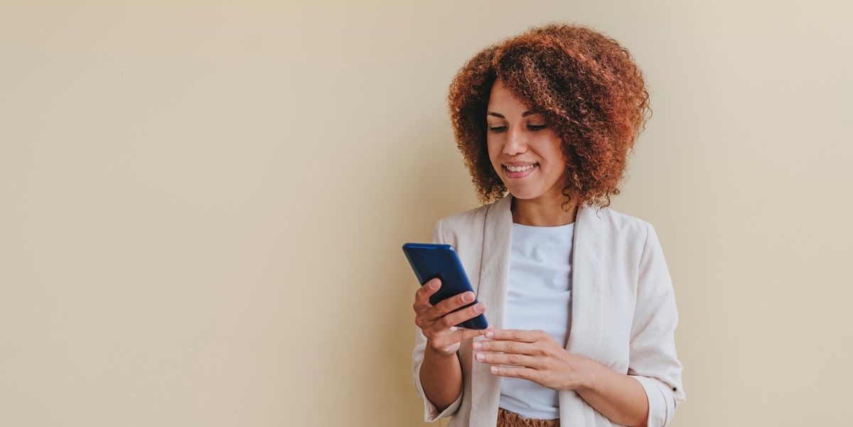 woman looking phone, standing in front of beige wall