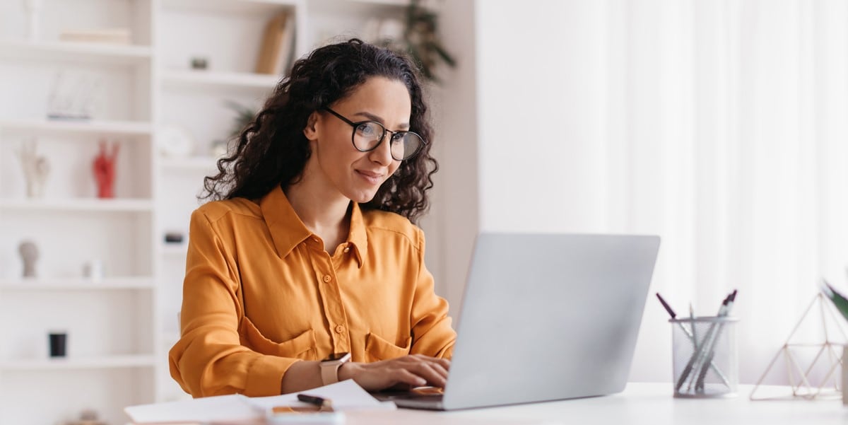 woman working at desk from home, using laptop