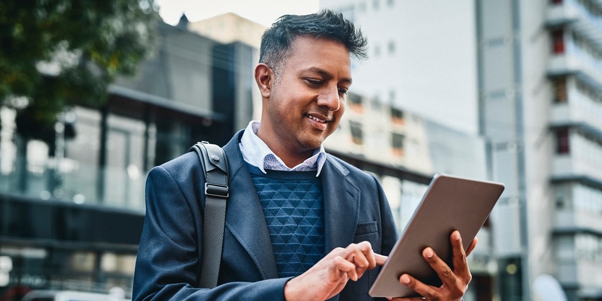 man standing outside, with bag, looking at tablet in hands