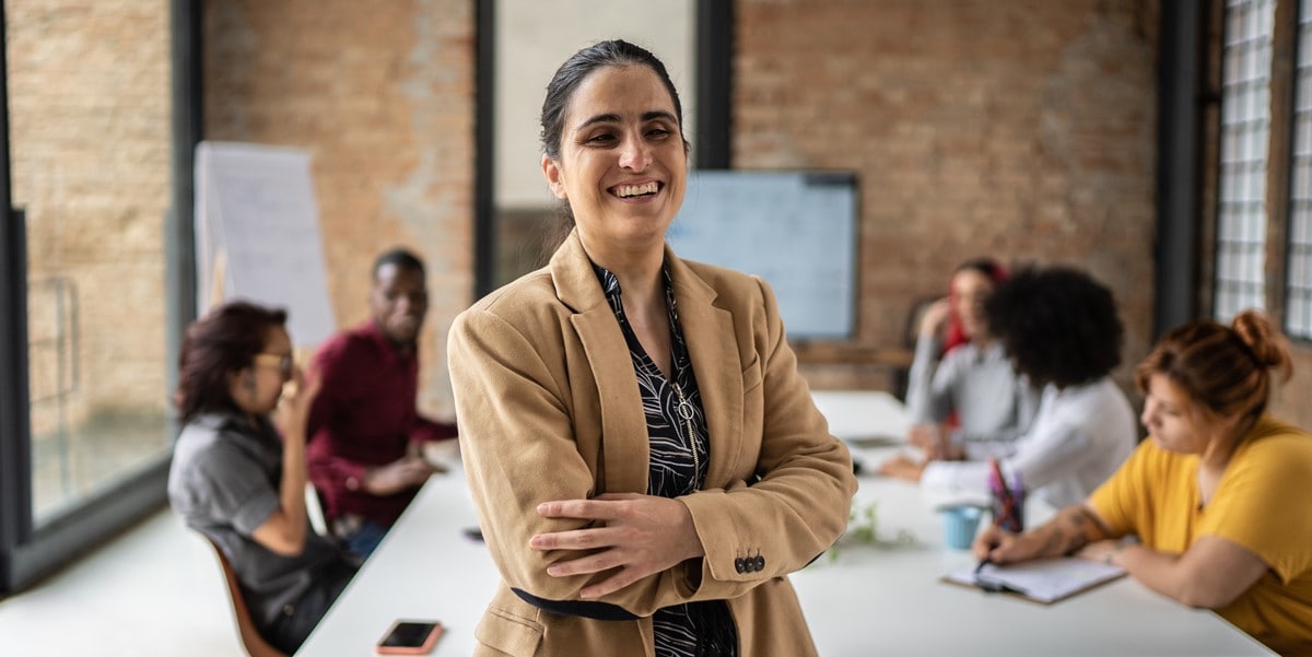 professional woman in office smiling, group of people at table in the background