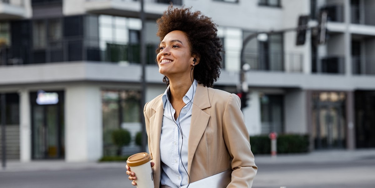 woman with coffee and laptop walking outside, in front of building