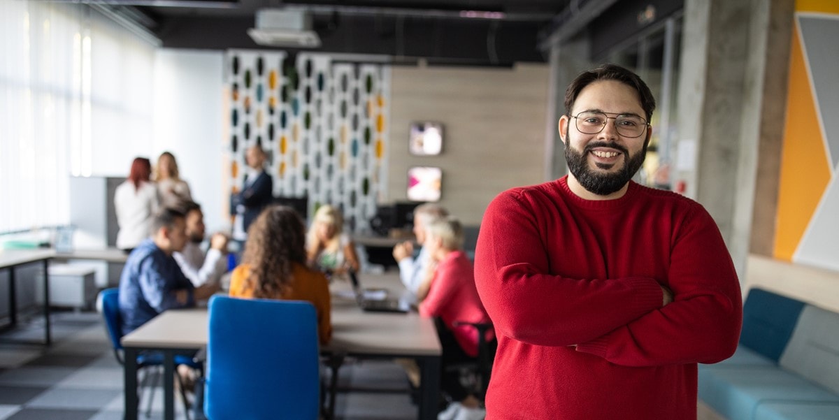 man with arms cross smiling, standing in front of conference table