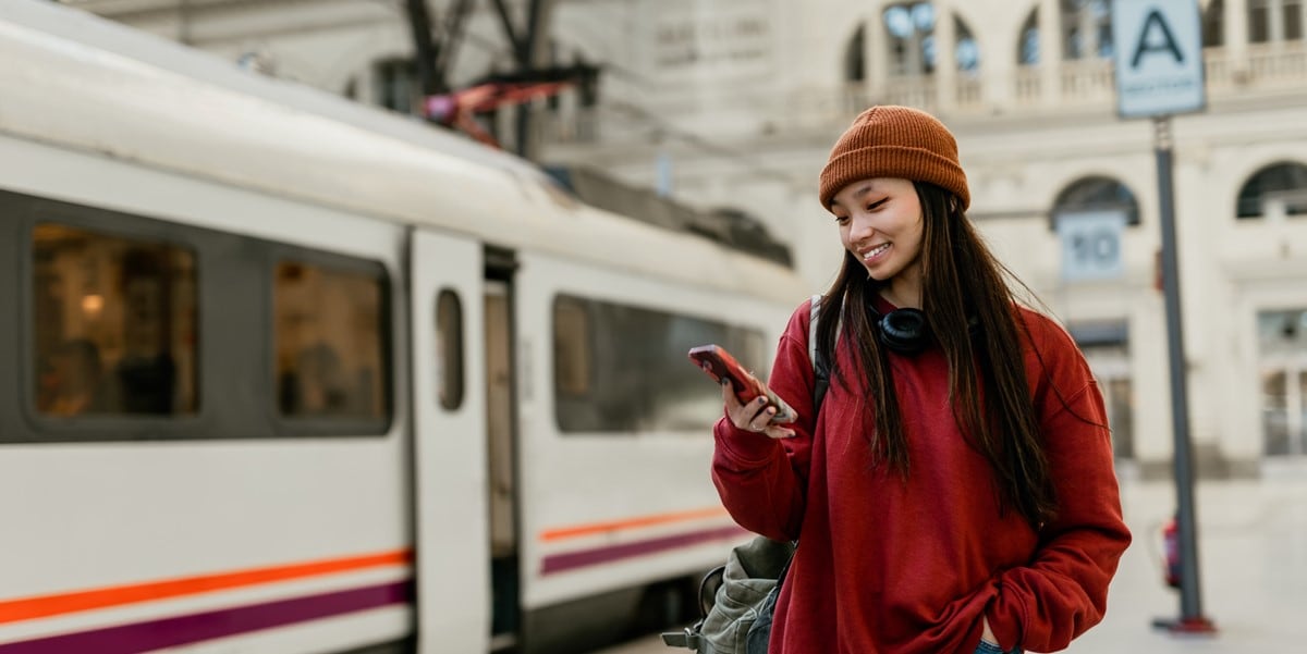 young woman next to bus, looking down at phone in hand